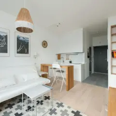 Jasne, nowoczesne wnętrze z białą kanapą, drewnianym blatem kuchennym i regałem. Idealne na Powiślu.