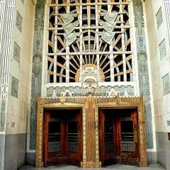 Monumentalny budynek w stylu art deco z ozdobnymi drzwiami i misternym oknem.