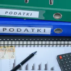 Dwa segregator "PODATKI", zeszyt, pieniądze i kalkulator. Jak zmniejszyć podatek za budynki gospodarcze?