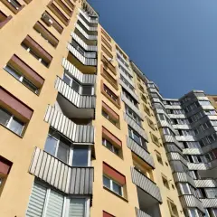 Żółty blok mieszkalny, typowe mieszkanie komunalne, z balkonami i oknami, na tle błękitnego nieba.