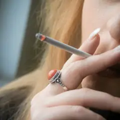 Zbliżenie na dłoń kobiety z zapalonym papierosem i pierścionkiem z koralami.