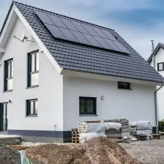 Nowy dom z panelami słonecznymi na dachu, materiały budowlane i żwir na placu budowy.