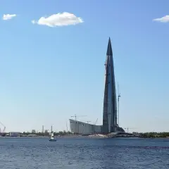 Lakhta Center, najwyższy budynek w Europie, wznosi się nad wodą. W tle widać inne budowy i żaglówkę.