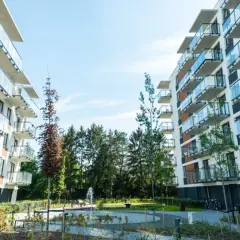 Nowoczesne apartamentowce z balkonami i szklanymi balustradami, otoczone zielenią. Idealne miejsce na inwestowanie w nieruchomości.
