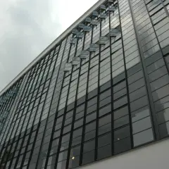 Fasada budynku w stylu modernizm, z rzędem przeszklonych okien i charakterystycznymi, wychylonymi świetlikami.