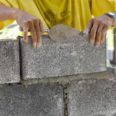 Murarz układa bloczek fundamentowy, sprawdzając jego wymiary.