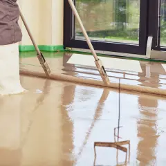Pracownik w gumowcach rozprowadza płynny **anhydryt** za pomocą łaty.