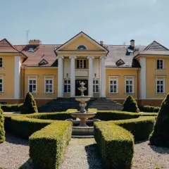 Żółty pałac z kolumnami i fontanną w ogrodzie.