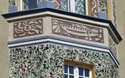 Sgraffito z rybą i abstrakcyjnymi kształtami na fasadzie budynku, ozdobionej mozaiką z kolorowego szkła.