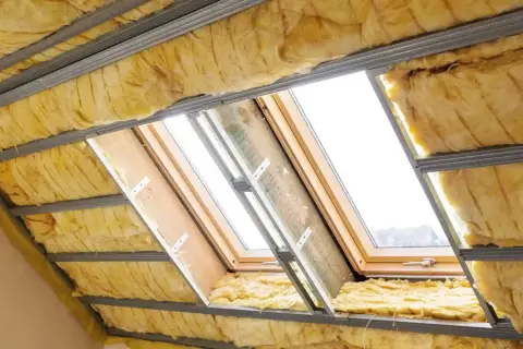 Ocieplenie dachu wełną mineralną w trakcie prac. Widoczne profile metalowe i żółta izolacja.
