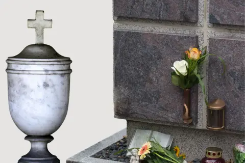 Kamienna urna z krzyżem i kwiaty przy ścianie kolumbarium.