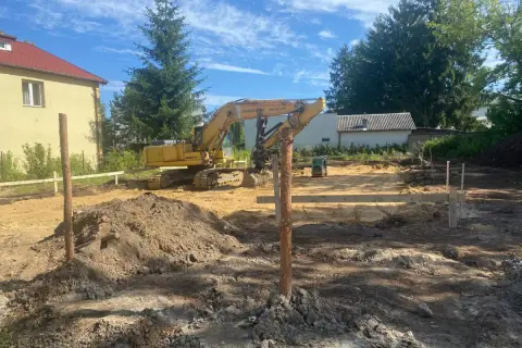 Plac budowy, gdzie koparka przygotowuje działkę budowlaną pod fundamenty.