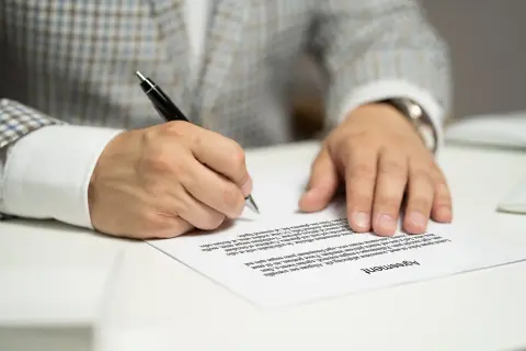 Mężczyzna w garniturze podpisuje umowę kredytową, składając ważny podpis na dokumencie.