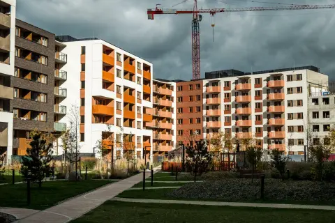 Nowe bloki mieszkalne z balkonami i żurawiem budowlanym w tle. Widać zielony dziedziniec, ścieżki i drzewa. Rynek wtórny w fazie rozwoju.
