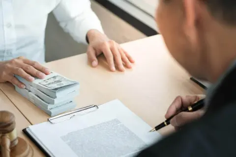 Stos banknotów dolarowych i dokumenty na biurku, sugerujące transakcję lub depozyt notarialny.