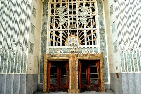 Monumentalny budynek w stylu art deco z ozdobnymi drzwiami i misternym oknem.