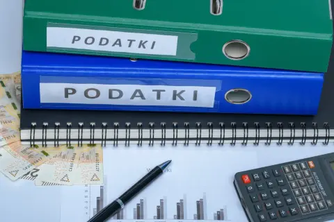 Dwa segregator "PODATKI", zeszyt, pieniądze i kalkulator. Jak zmniejszyć podatek za budynki gospodarcze?