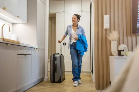 Uśmiechnięta kobieta z walizką w nowoczesnym mieszkaniu, gotowa na przeprowadzkę. To musi być najlepsza umowa najmu mieszkania!