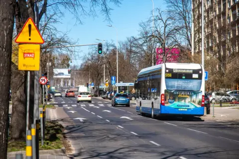 Korytarz miejski z ruchem ulicznym, autobusem i samochodami. Znaki drogowe ostrzegają przed wyjazdem.