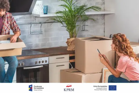 Para urządzająca kuchnię, przygotowująca meldunek tymczasowy. Kartony i rośliny tworzą atmosferę przeprowadzki.