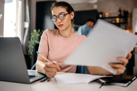 Kobieta w okularach pracuje nad dokumentami, przygotowując wykreślenie hipoteki. Obok laptop i notatnik.
