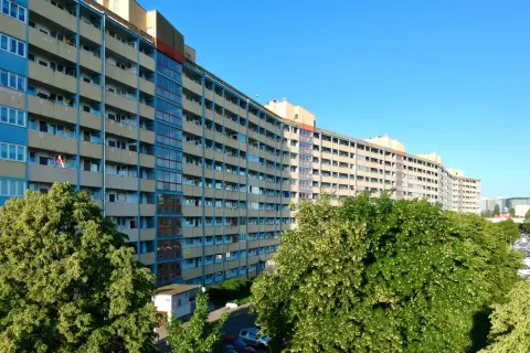 Długi, falisty budynek mieszkalny w Gdańsku, z balkonami i oknami, otoczony zielenią.