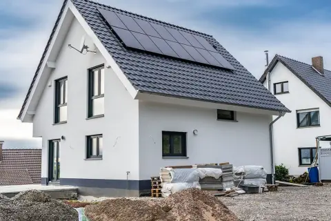 Nowy dom z panelami słonecznymi na dachu, materiały budowlane i żwir na placu budowy.