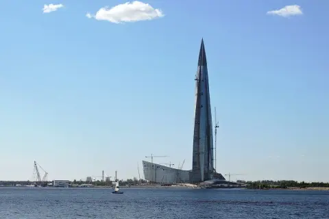 Lakhta Center, najwyższy budynek w Europie, wznosi się nad wodą. W tle widać inne budowy i żaglówkę.