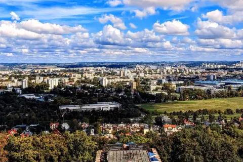 Widok na rozległe osiedla Krakowa, gdzie ceny mieszkań mogą być wysokie. W oddali widać zabudowania i zieleń.