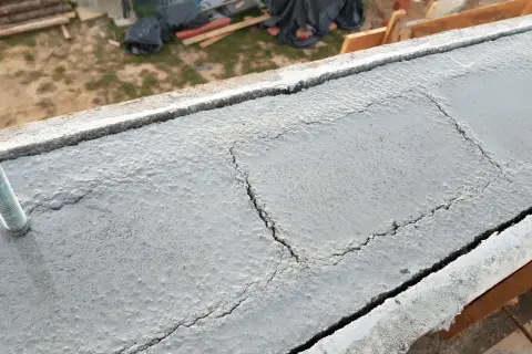 Pęknięty wieniec budowlany z widocznym prętem. Na tle plac budowy.