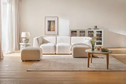 Przytulny salon z kanapą i pufą w odcieniach beżu. Beżowy kolor ścian tworzy ciepłą atmosferę.