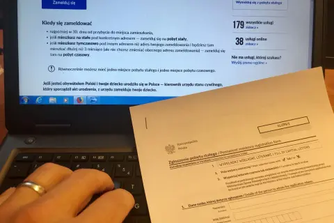Dłoń na klawiaturze laptopa, obok formularz "Zgłoszenie pobytu stałego". Obowiązek meldunkowy w praktyce.