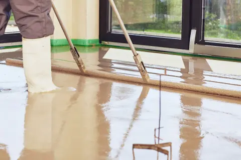 Pracownik w gumowcach rozprowadza płynny **anhydryt** za pomocą łaty.