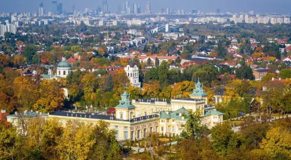 Pałac wilanowski otoczony jesiennym parkiem, z panoramą Warszawy w tle. To symbol najbogatszej dzielnicy Warszawy.