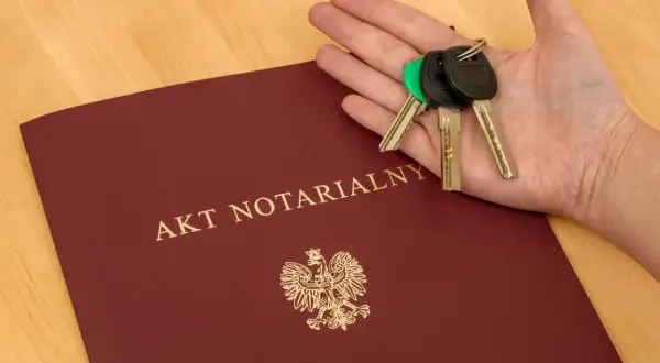 Dłoń z kluczami spoczywa na okładce dokumentu "AKT NOTARIALNY", symbolizując finalizację zakupu mieszkania.