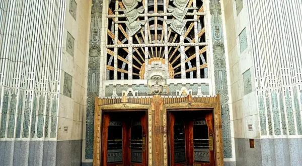 Monumentalny budynek w stylu art deco z ozdobnymi drzwiami i misternym oknem.