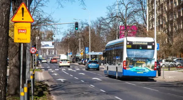Korytarz miejski z ruchem ulicznym, autobusem i samochodami. Znaki drogowe ostrzegają przed wyjazdem.