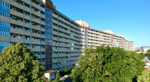 Długi, falisty budynek mieszkalny w Gdańsku, z balkonami i oknami, otoczony zielenią.