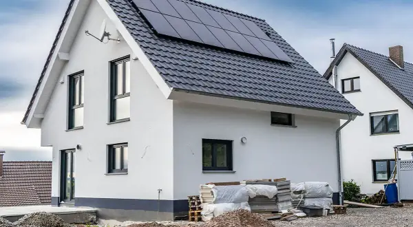 Nowy dom z panelami słonecznymi na dachu, materiały budowlane i żwir na placu budowy.