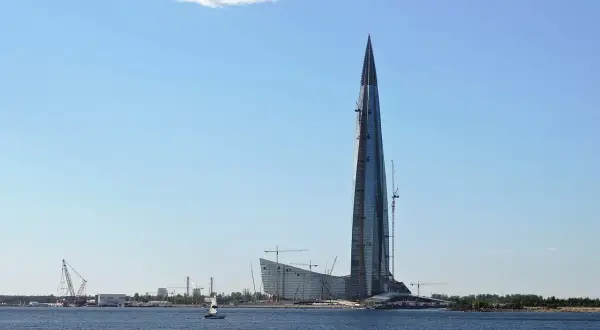 Lakhta Center, najwyższy budynek w Europie, wznosi się nad wodą. W tle widać inne budowy i żaglówkę.