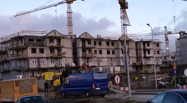 Budowa bloków mieszkalnych w Gdańsku. W tle dźwigi budowlane, na pierwszym planie samochody i maszyny budowlane. Ceny mieszkań gdańsk mogą być wysokie.