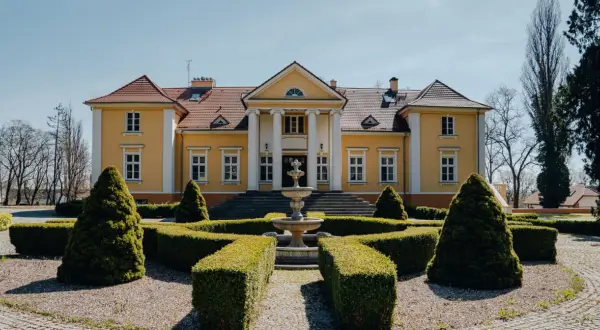 Żółty pałac z kolumnami i fontanną w ogrodzie.