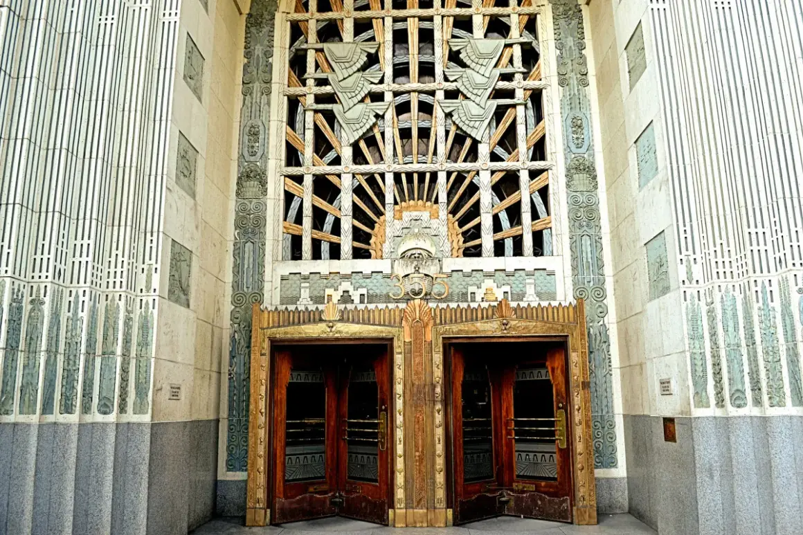 Monumentalny budynek w stylu art deco z ozdobnymi drzwiami i misternym oknem.