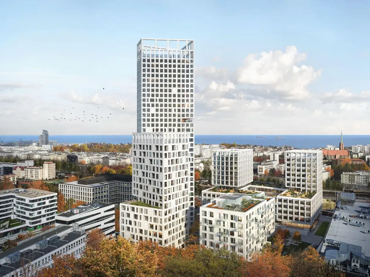 Nowoczesna architektura miasta z białymi wieżowcami i budynkami mieszkalnymi, otoczona jesienną zielenią i błękitnym morzem.
