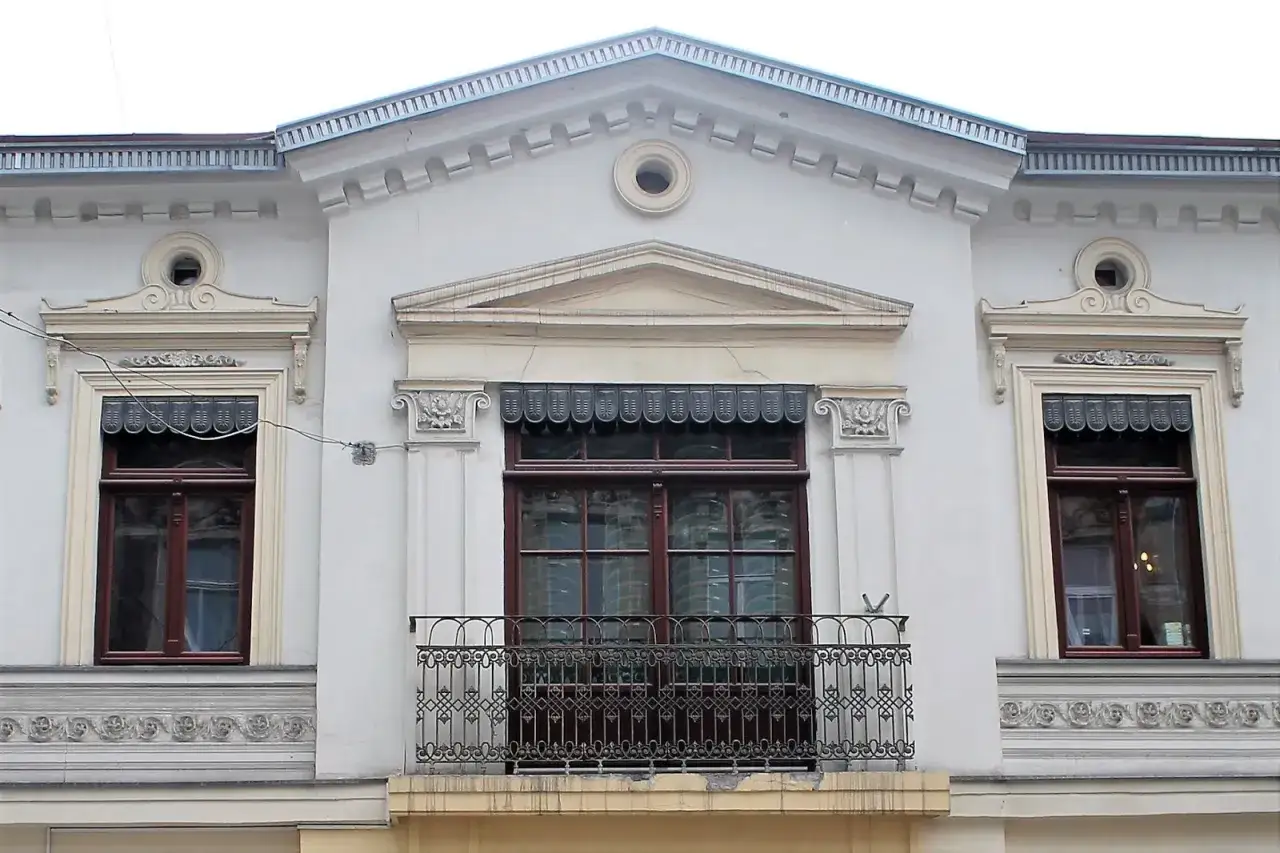 Elegancki fronton kamienicy z balkonem i ozdobnymi oknami.