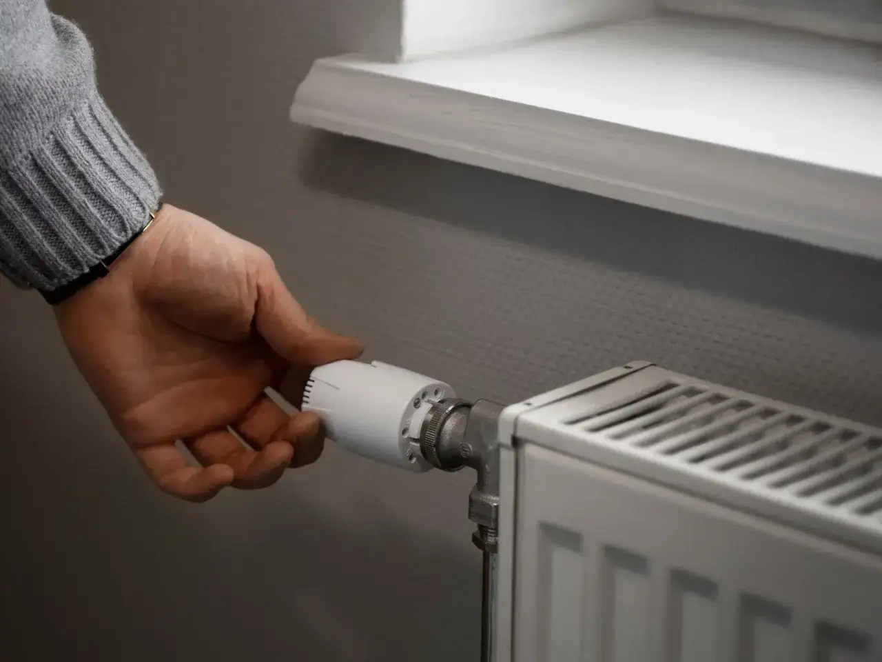 Dłoń reguluje termostat grzejnika. Dowiedz się, jak ustawić grzejnik w bloku, by cieszyć się komfortem i oszczędzać energię.
