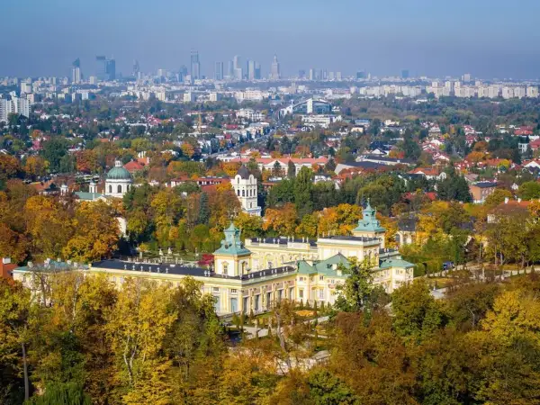 Pałac wilanowski otoczony jesiennym parkiem, z panoramą Warszawy w tle. To symbol najbogatszej dzielnicy Warszawy.