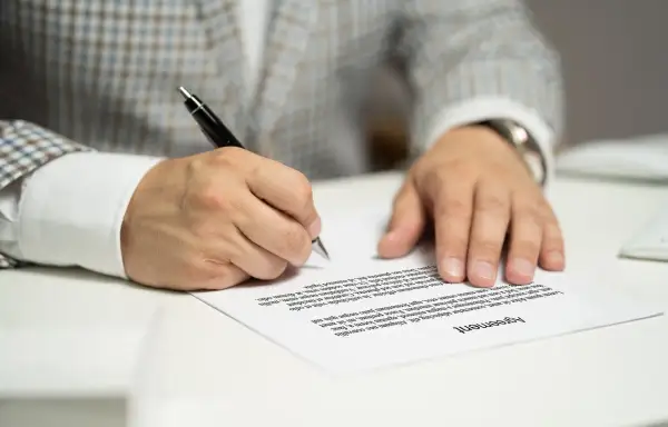 Mężczyzna w garniturze podpisuje umowę kredytową, składając ważny podpis na dokumencie.