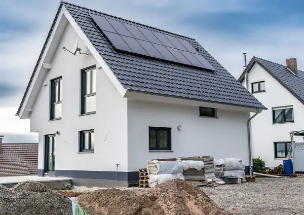 Nowy dom z panelami słonecznymi na dachu, materiały budowlane i żwir na placu budowy.