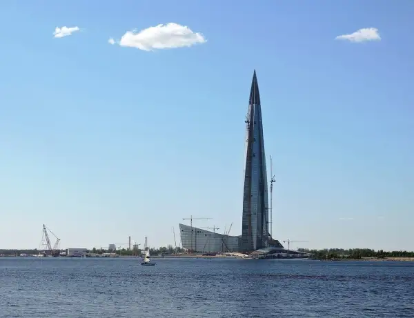 Lakhta Center, najwyższy budynek w Europie, wznosi się nad wodą. W tle widać inne budowy i żaglówkę.